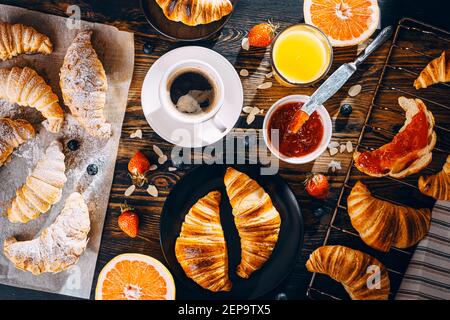 Das Konzept eines großen und abwechslungsreichen Frühstück. Verschiedene Croissants und Marmeladen, Kaffee und Amelsin Saft, Grapefruit und Erdbeeren auf der Tischplatte vie Stockfoto