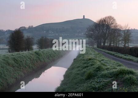 Sonnenaufgang über einem nebligen Fluss, der in Richtung Glastonbury Tor, Somerset, Großbritannien, führt. Stockfoto