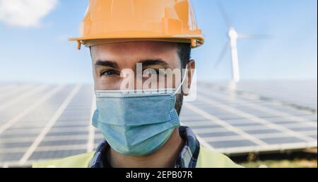 Junger Mann, der im Solarkraftwerk arbeitet und dabei Sicherheit trägt Gesichtsmaske für Coroanvirus Ausbruch - Eco-Konzept - weich Fokus auf Augen Stockfoto