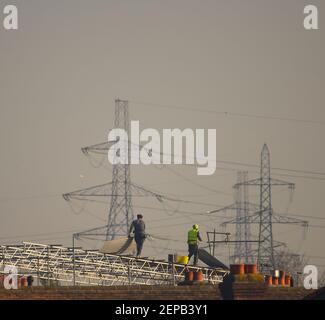 Merton Park, London, Großbritannien. 27. Februar 2021. Männer arbeiten auf dem Dach eines Home Loft Umwandlung in hellem Sonnenlicht vor einem Hintergrund von entfernten Power Pylons. Quelle: Malcolm Park/Alamy Live News. Stockfoto