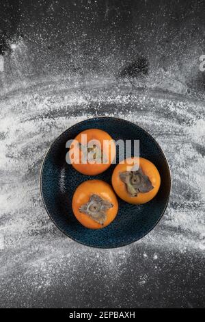 Schwarze Platte mit reifen Kaki-Früchten auf schwarzer Oberfläche Stockfoto