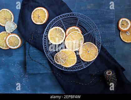 Draufsicht auf ein Kühlregal mit einigen getrockneten Limetten und Orangen oben. Eine elegante blaue Serviette und mehr Zitrusscheiben stehen auf einem Holztisch. Stockfoto