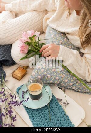 Frau in Wolle Loungewear gekleidet hält einen Blumenstrauß mit ihren Händen, während sie auf dem Bett liegt. Stockfoto