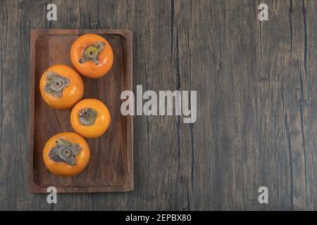Teller mit leckeren fuyu-Kaki-Früchten auf Holzoberfläche Stockfoto