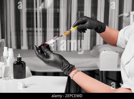 Die Hände des Kosmetologen in schwarzen Gummihandschuhen während des Befüllens der Spritze mit Plasma aus einem Blutschlauch. Schönheitssalon. Konzept der modernen Schönheitsbehandlung Stockfoto