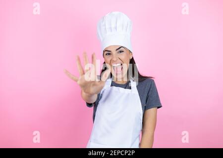 Junge hispanische Frau trägt Bäckeruniform über rosa Hintergrund zeigt Und mit den Fingern Nummer fünf nach oben zeigen und dabei selbstbewusst lächeln Und glücklich Stockfoto