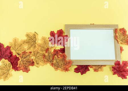 Leerer Holzrahmen auf gelbem Hintergrund mit Herbstblättern. Flach liegend. Speicherplatz kopieren. Draufsicht Stockfoto