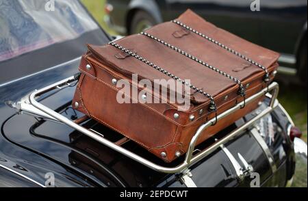 Nahaufnahme eines Vintage-braunen Reisekoffers, auf einem glänzenden Chromrahmen auf der Rückseite eines schwarzen Oldtimers umschnallt. Stockfoto