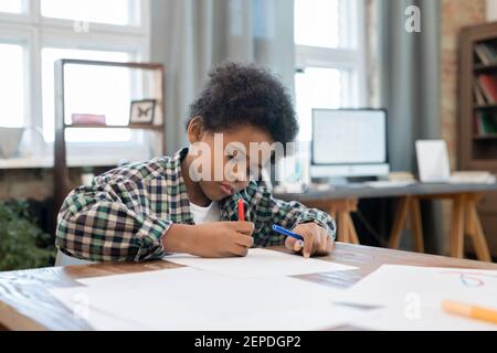 Fleißig Schuljunge in Casualwear Zeichnung mit Textmarker auf Papier durch Tisch im Wohnzimmer, während Sie nach Hausaufgaben die Freizeit genießen Stockfoto