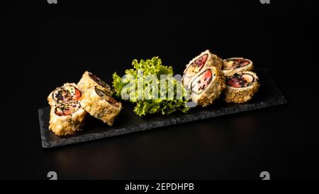 Benutzerdefinierte Sushi-Rolle in Tempura mit Nori, frischem Lachs, Thunfisch, Avocado, Masago-Kaviar, beträufelt mit Ananassauce mit Salat gießen als Dekoration auf Stockfoto