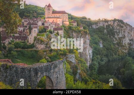 Sonnenuntergang oder Sonnenaufgang Blick auf den malerischen Hügel mittelalterlichen Französisch Dorf Saint-Cirq-Lapopie, Frankreich mit der befestigten Kirche beleuchtet über dem Lot Stockfoto