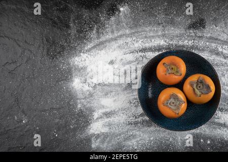 Schwarze Platte mit reifen Kaki-Früchten auf schwarzer Oberfläche Stockfoto