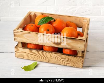 Holzkiste mit süßen reifen orangen Mandarinen auf einem Küchentisch. Frische Zitrusfrüchte in Holzkiste. Umweltfreundliche Behälter im rustikalen Stil für Obst und Gemüse Stockfoto