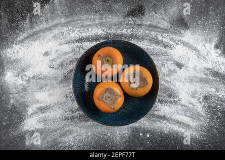Schwarze Platte mit reifen Kaki-Früchten auf schwarzer Oberfläche Stockfoto