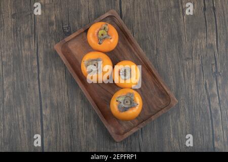 Teller mit leckeren fuyu-Kaki-Früchten auf Holzoberfläche Stockfoto