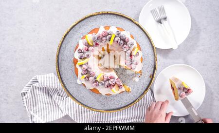 Flach liegend. Schritt für Schritt. Schneiden von Zitrone Cranberry Bundt Kuchen mit Zucker Cranberries und Zitronenkeile verziert. Stockfoto