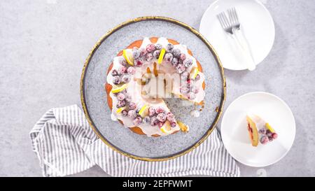 Flach liegend. Schritt für Schritt. Schneiden von Zitrone Cranberry Bundt Kuchen mit Zucker Cranberries und Zitronenkeile verziert. Stockfoto