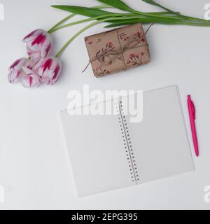 Draufsicht auf Tulpen, Geschenk und leeren Notizblock auf weißem Hintergrund Stockfoto