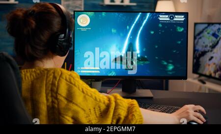 Pro Gamer spielt im Weltraum-Shooter auf dem PC. Frauen spielen mit Teamkollegen über Kopfhörer während Online-eSport-Turnier in Aktion mit Technologie Netzwerk drahtlos aufgenommen Stockfoto