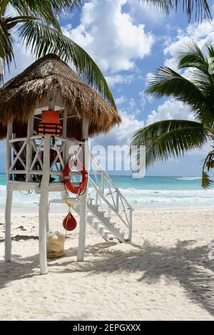 Rettungsschwimmer Turm am Caribbean Beach, mit flachem Sand, Palmen um und das türkisfarbene Meer. Im Hintergrund der wolkige Himmel und der Ozean Stockfoto