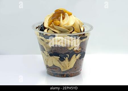 Dessert mit Schokolade und Karamell Mousse in einem Plastikglas. Schokoladen-Biskuit mit Schlagsahne bestreut mit Nüssen. Desserts zum Mitnehmen im Dispo Stockfoto