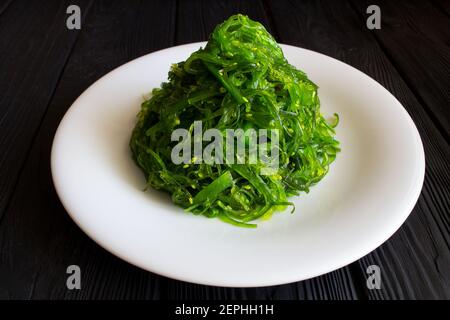 Salat mit Algen und Sesam auf dem weißen Teller Der schwarze Holzhintergrund Stockfoto