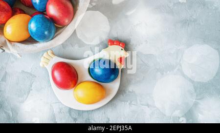 Osterkomposition. Bemalte bunte Eier in einem Keramik-Huhn mit einem Bouquet von frühlingsgelben Mimosen auf dem Ostertisch. Speicherplatz kopieren. Stockfoto