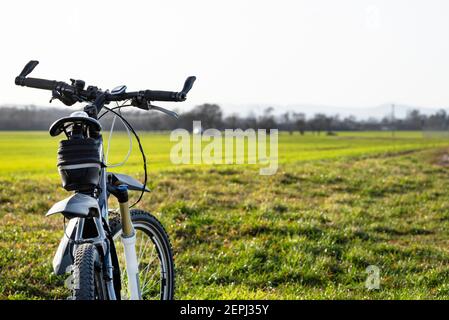 Ein Fahrradlenker aus der Perspektive der ersten Person. Sichtbarer Fahrradrahmen und Fahrradzubehör am Lenker und am Feld im Rückenbereich Stockfoto