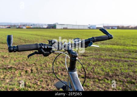 Ein Fahrradlenker aus der Perspektive der ersten Person. Sichtbarer Fahrradrahmen und Fahrradzubehör am Lenker und am Feld im Rückenbereich Stockfoto