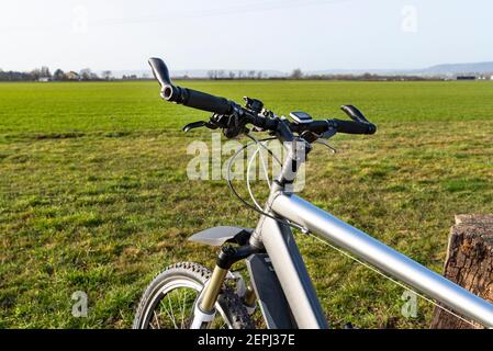 Ein Fahrradlenker aus der Perspektive der ersten Person. Sichtbarer Fahrradrahmen und Fahrradzubehör am Lenker und am Feld im Rückenbereich Stockfoto