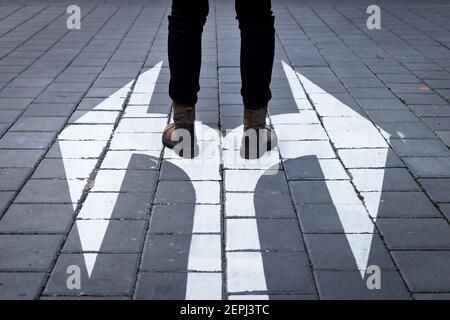 Treffen Sie die Entscheidung, welchen Weg zu gehen. Zu Fuß am Richtungsschild auf der Straße. Auswahlkonzept mit menschlichen Beinen und Pfeil-Symbol auf der Straße Stockfoto