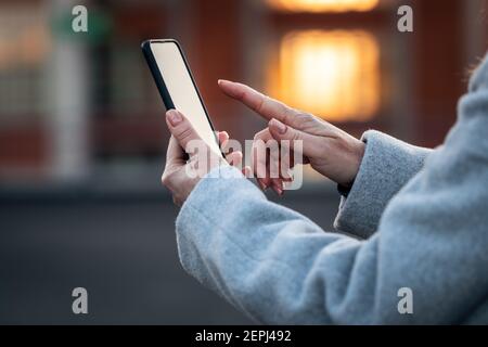 Frau, die ihr Mobiltelefon auf der Straße der Stadt benutzt. Smartphone in weiblicher Hand. Mit der mobilen App und Verbindung zum Internet im Freien Stockfoto