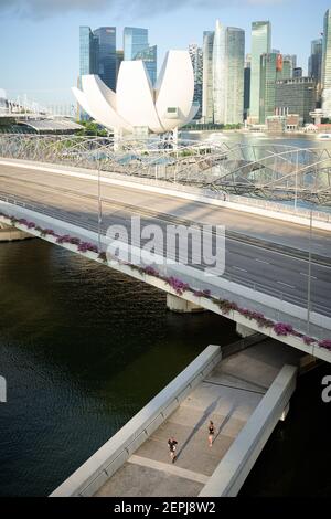 Singapur - 24 Jun 2019: Zwei Läufer joggen bei Sonnenaufgang auf einer Fußgängerbrücke unter der Sheares Avenue vor dem ArtScience Lotus-förmigen Museum an Stockfoto