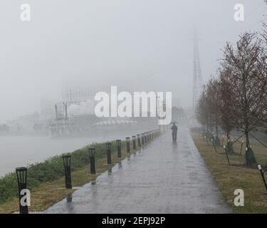 Silhouettenfiguren mit Regenschirmen spazieren entlang des nebelverhangenen Mississippi-Flussufers, vorbei am historischen Dampfschiff Natchez in New Orleans. Stockfoto