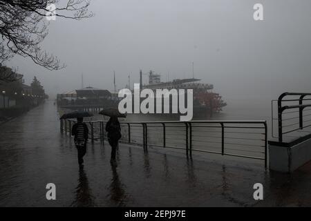 Silhouettenfiguren mit Regenschirmen spazieren entlang des nebelverhangenen Mississippi-Flussufers, vorbei am historischen Dampfschiff Natchez in New Orleans. Stockfoto