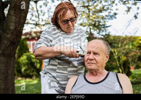 Bleiben Sie zu Hause, bleiben Sie sicher und positiv und kümmern sich um sich selbst innerhalb der gleichen Familie während Coronavirus Lockdown. Ältere Paar macht Frisur jeder ot Stockfoto