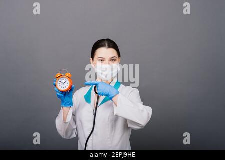 Lächelnde Ärztin Frau in Maske zeigt auf Uhr, Zeit zu impfen, medizinische Konzept Stockfoto