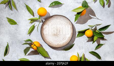 Ganze Orangen mit Orangenbaumblättern auf weißem Hintergrund um leeren Teller. Draufsicht, Flachlage, Sommer und gesundes Konzept. Modell Stockfoto