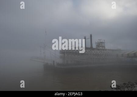 Silhouettenfiguren mit Regenschirmen spazieren entlang des nebelverhangenen Mississippi-Flussufers, vorbei am historischen Dampfschiff Natchez in New Orleans. Stockfoto