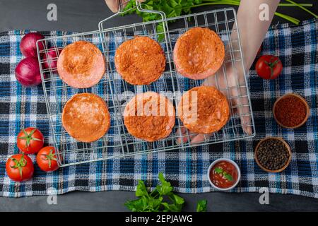Weibliche Hand hält gegrillte Salami-Scheiben auf dem Grillrost über Frisches Gemüse Stockfoto