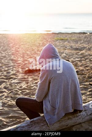 Sad und einsamer Mann in einem Hoodie sitzen auf dem Melden Sie sich bei Seaside an Stockfoto