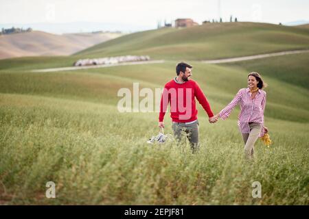Ein junges, fröhliches Paar, das sich glücklich fühlt, während es an einem schönen Tag auf einer großen Wiese zusammen geht. Liebe, Beziehung, zusammen, Natur Stockfoto