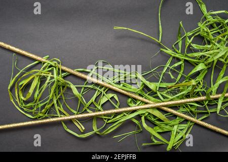 Schöner Hintergrund. Grüner Bast liegt auf schwarzem Hintergrund. Auf dem Bast befinden sich auch zwei dekorative Stäbchen Stockfoto