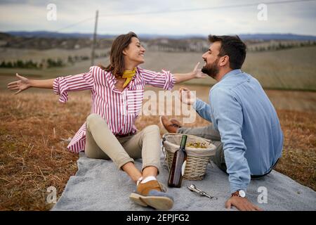 Ein junges Paar genießt Momente des Hedonismus mit Trauben und Wein auf dem Picknick auf einer großen Wiese an einem schönen Tag. Beziehung, zusammen, Liebe, Stockfoto