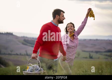 Ein junges Paar, das die Natur genießt, während es an einem schönen Tag auf einer großen Wiese spazierengeht. Beziehung, Liebe, zusammen, Picknick Stockfoto