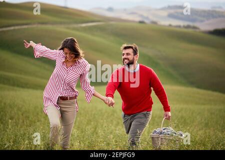 Ein junges Paar genießt die Natur beim Wandern auf einer großen Wiese, indem es die Hände an einem schönen Tag hält. Beziehung, Liebe, zusammen, Picknick, Natur Stockfoto