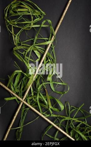 Schöner Hintergrund. Grüner Bast liegt auf schwarzem Hintergrund. Auf dem Bast befinden sich auch zwei dekorative Stäbchen Stockfoto