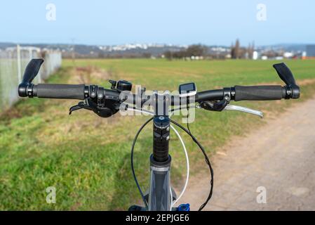 Mountainbike-Lenker aus der Perspektive der ersten Person gesehen. Sichtbarer Fahrradrahmen und Fahrradzubehör auf dem Lenker und dem Feld in der BA Stockfoto