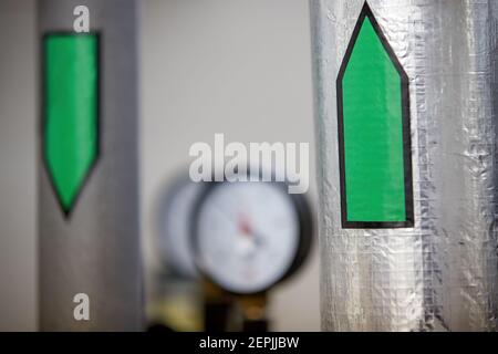 Zentralheizung. Thermometer an der Warmwasserzuleitung zum Heizsystem. Techniker trägt rote Jacke mit weißem Helm. Stockfoto