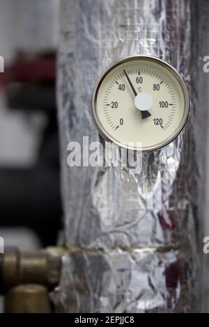 Zentralheizung. Thermometer an der Warmwasserzuleitung zum Heizsystem. Techniker trägt rote Jacke mit weißem Helm. Stockfoto